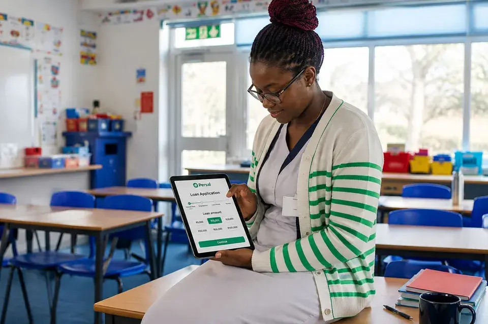 A teacher in her classroom reviewing a Persal loan application on a tablet